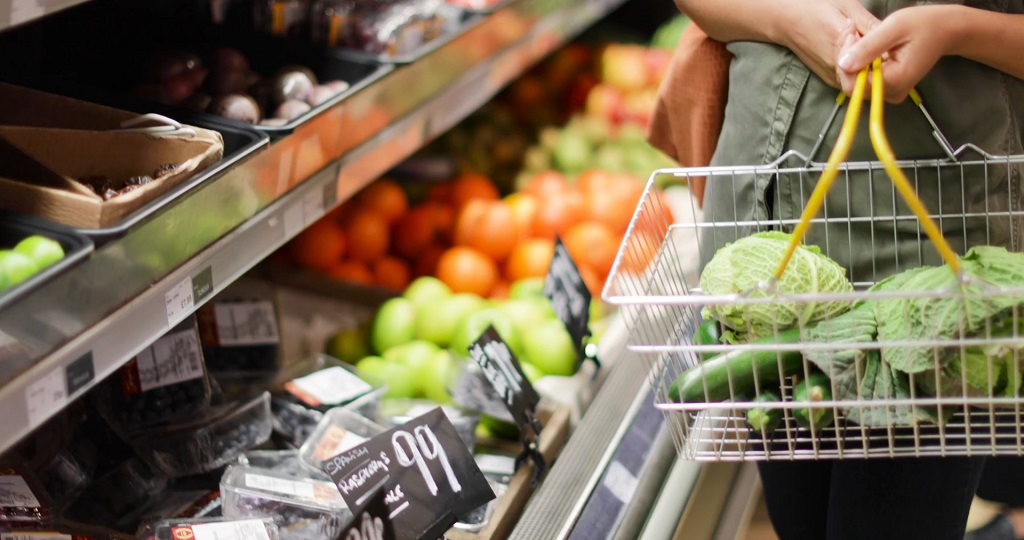 Close-up of a grocery basket filled with fresh vegetables in front of produce shelves