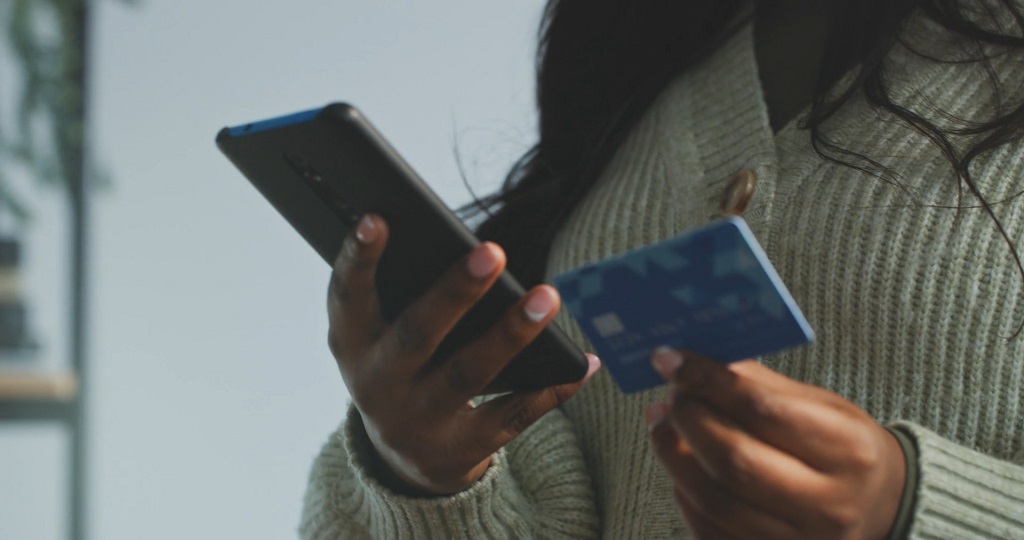 Person holding a credit card and smartphone, making an online purchase