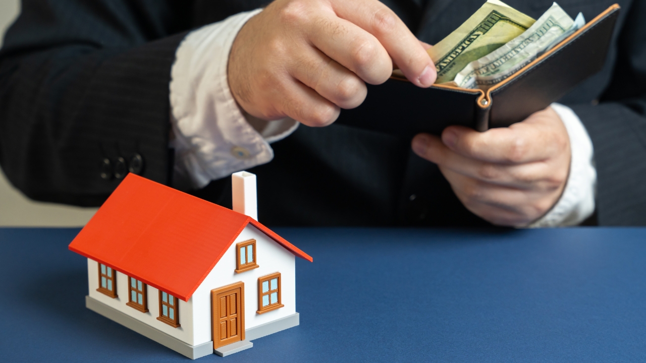 Person holding cash from a wallet next to a small model house on a table