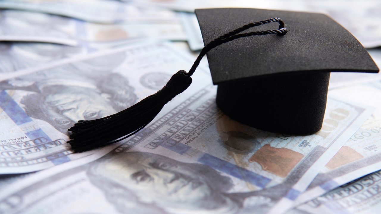 Graduation cap on US dollar bills showing how education affects salary levels