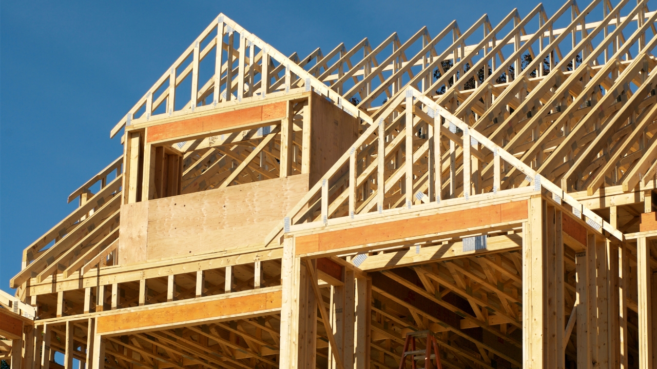 Wooden house frame under construction with roof trusses in place on a clear day