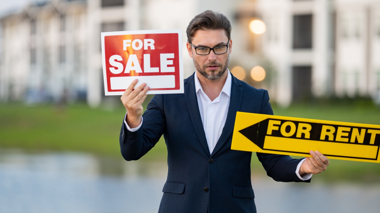 Man holds for sale and for rent signs outside a property