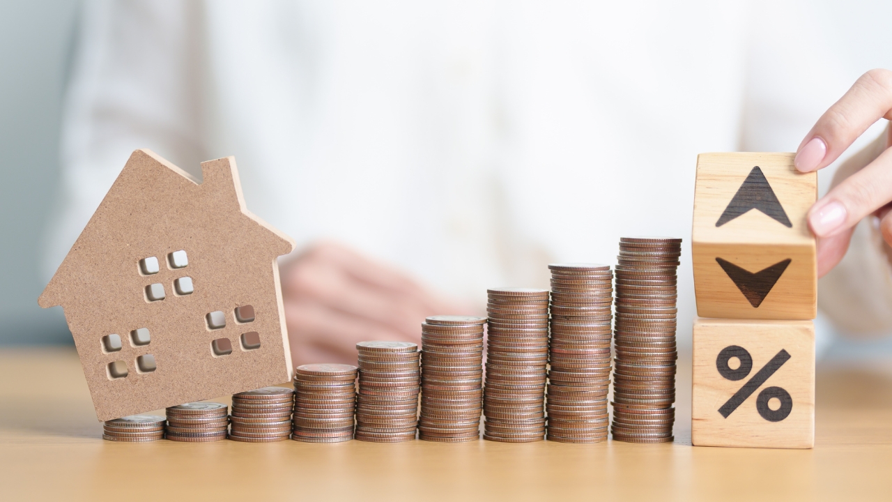 House model and coin stacks illustrate current mortgage rates and loan cost changes