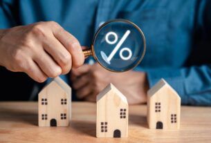 A person checks mortgage rates with a magnifying glass above small wooden houses