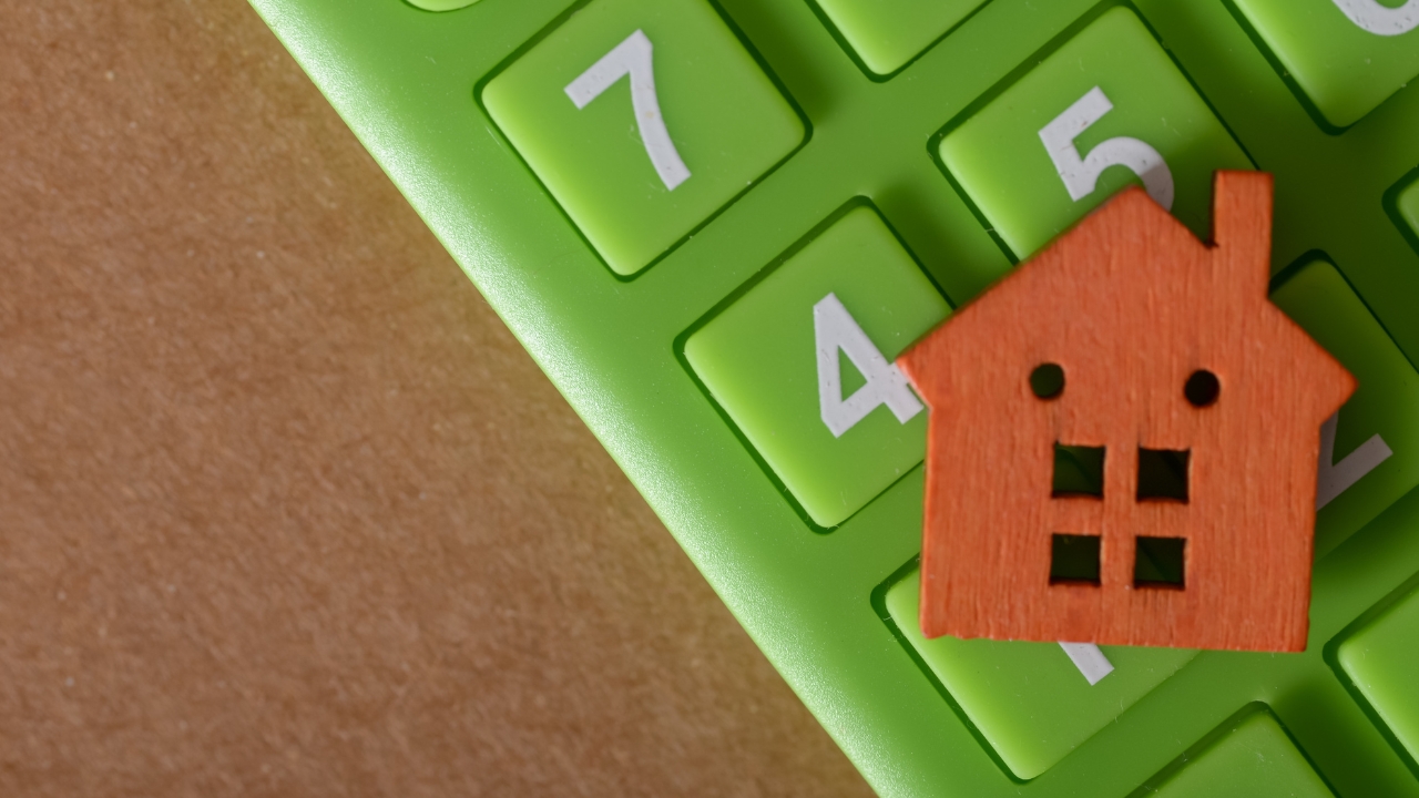 Small red house model sits on a calculator for a rent and mortgage cost guide