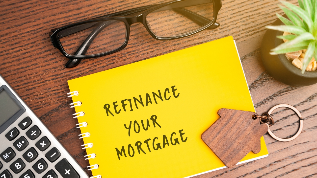A refinance note sits beside a calculator, glasses, and a house keychain